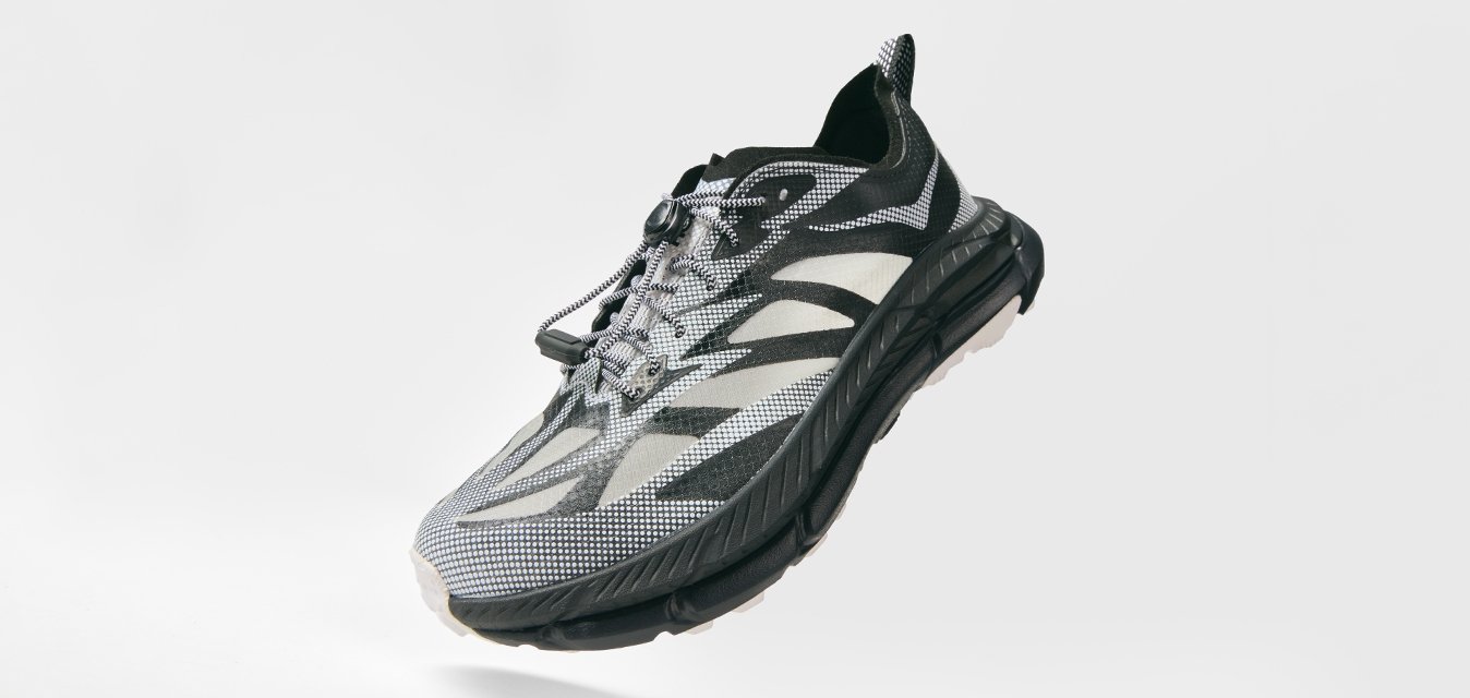 Scarpa sportiva nera e grigia con tomaia in rete pattern, lacci sicuri, suola spessa e ammortizzata, mostrata in angolo su uno sfondo bianco.