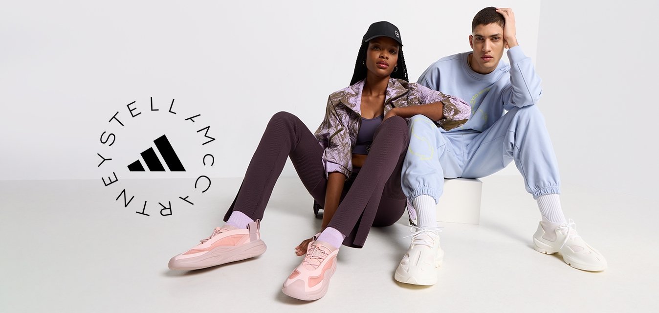 Due modelli seduti su una superficie chiara. Uno indossa un giacca marrone a fantasia, leggings viola e scarpe da ginnastica rosa. L'altro indossa un tuta blu chiaro e scarpe da ginnastica bianche.