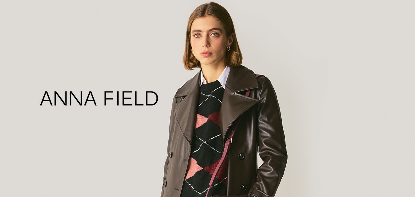 Cappotto trench in pelle marrone con ampio colletto e design doppiopetto, abbinato a un maglione nero a motivi e a una borsa in pelle di coccodrillo color amaranto.