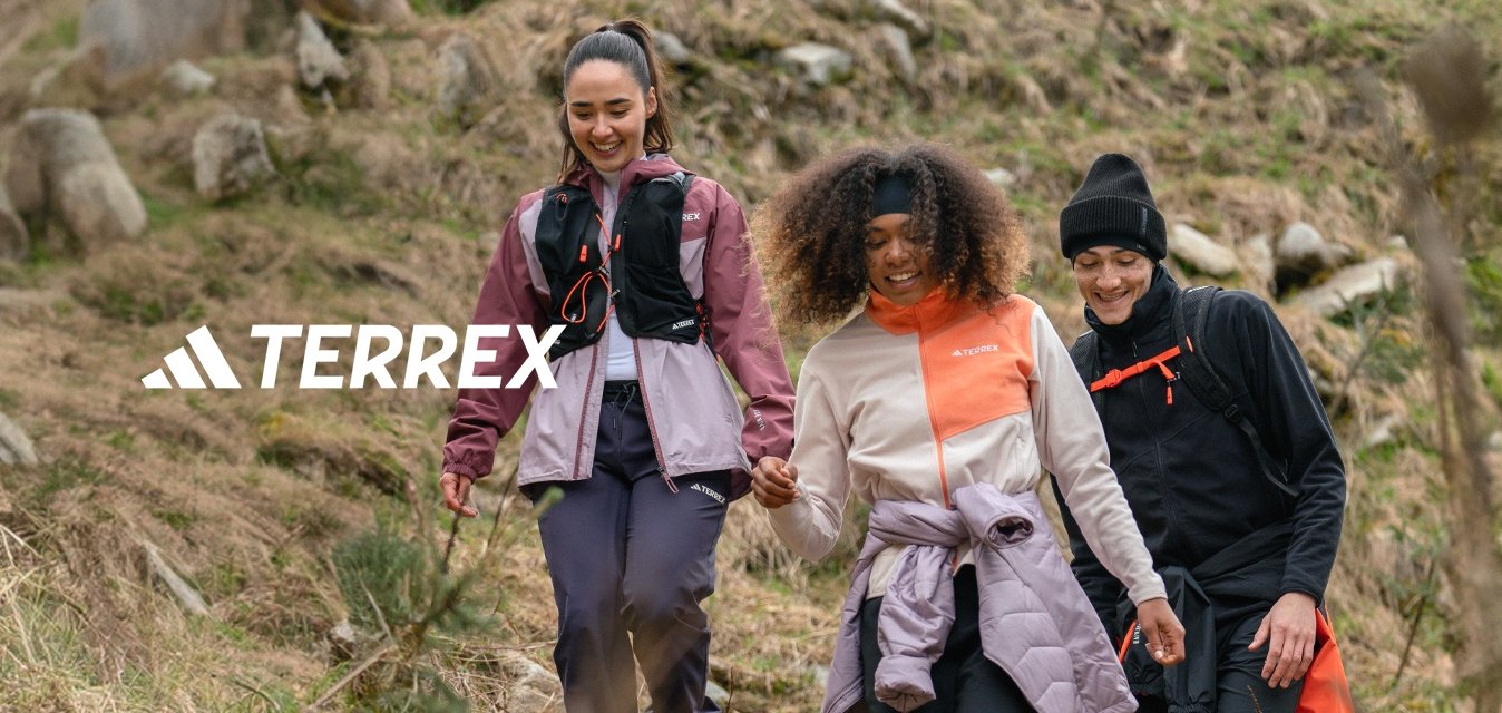 Tre persone camminano su una pendice erbosa. Indossano abbigliamento da esterno: giacche di colore viola, bianco e nero, con diverse trame e leggings.