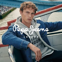 Giacca di jeans sopra una felpa grigia con testo, pantaloni scuri. Sedia metallica curva in una gondola sulla ruota panoramica, sullo sfondo si vedono la città e il fiume.