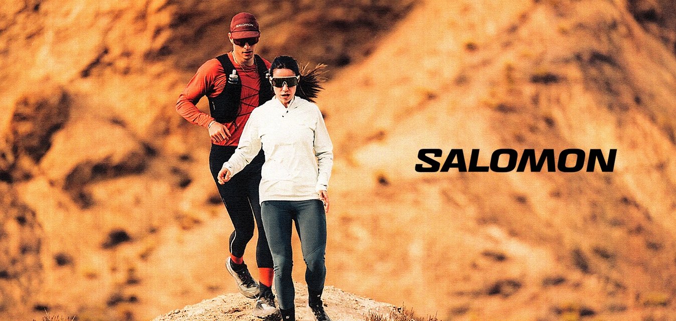 Due corridori percorrono un sentiero roccioso. Il maschio indossa una maglietta rossa e attrezzatura nera, mentre la femmina ha una maglietta bianca a maniche lunghe e leggings scuri.