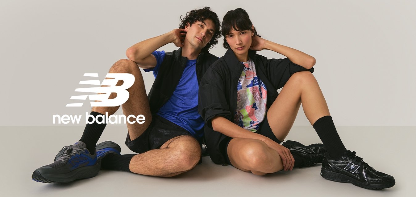 Due giovani adulti seduti per terra con le gambe piegate, vestiti con abbigliamento sportivo casual e scarpe da ginnastica, su uno sfondo chiaro e semplice.