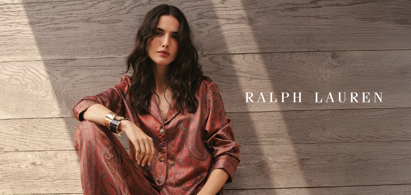 Set di pigiami in raso rosso con motivo paisley, bottoni frontali, maniche lunghe e vestibilità rilassata, abbinato a un semplice braccialetto con polsino, su un ponte di legno.