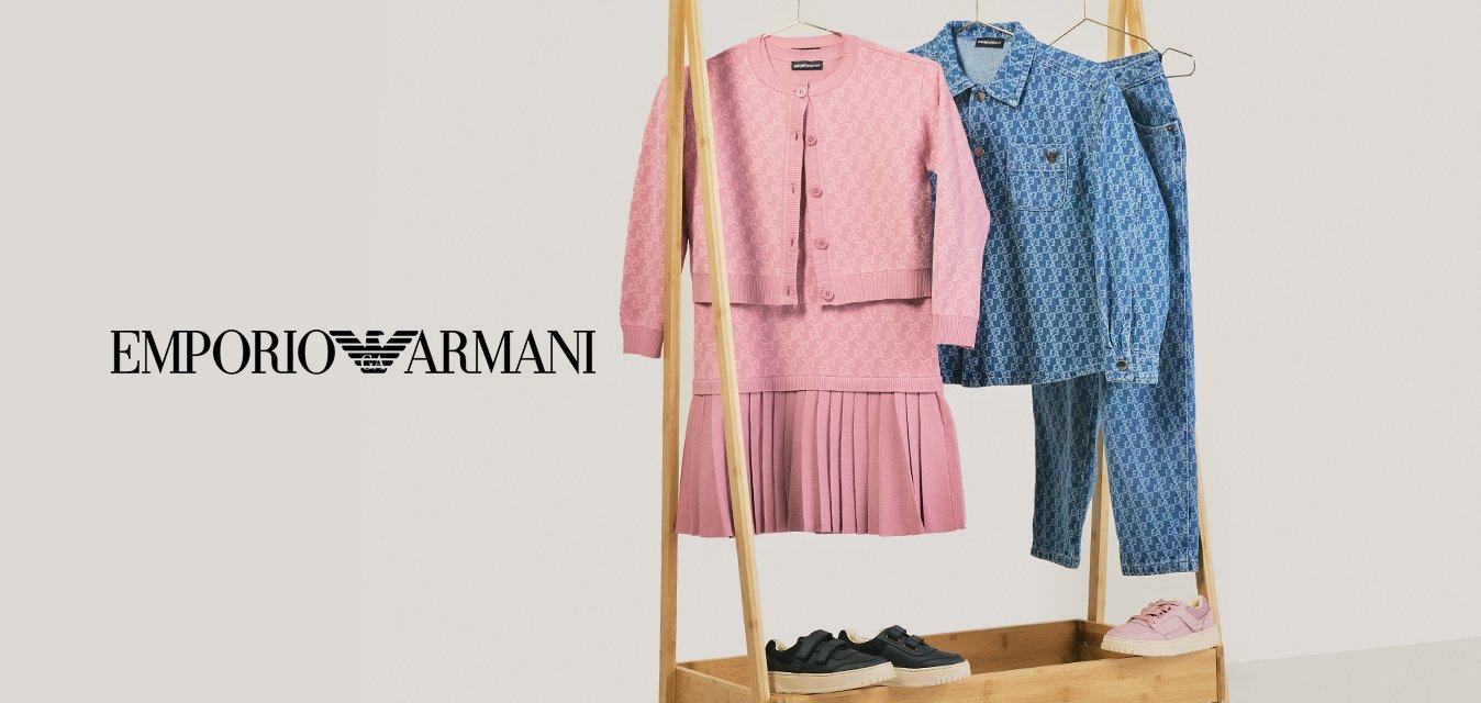 Stendino per abiti in legno con vestito lavorato a maglia rosa e cardigan, camicia blu a fantasia e jeans, sneaker nere e rosa sopra e sotto il rack.
