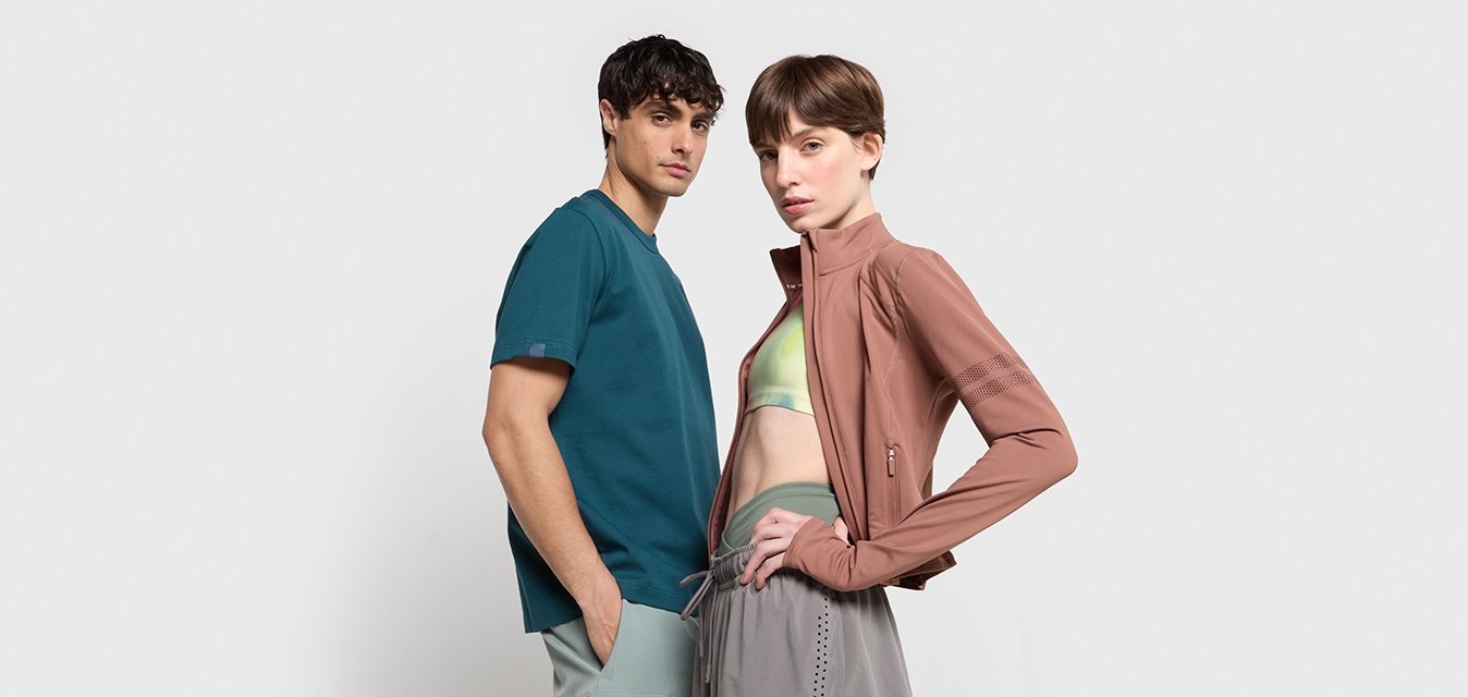 Maglietta teal a maniche corte e reggiseno sportivo verde chiaro abbinati a una giacca rosa aderente con zip e pantaloni sportivi grigi con accenti a fantasia.