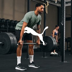 Cinque persone che si allenano in una palestra; uno solleva un bilanciere, gli altri utilizzano palle mediche o attrezzature da palestra in un'area di allenamento ampia e ben illuminata.