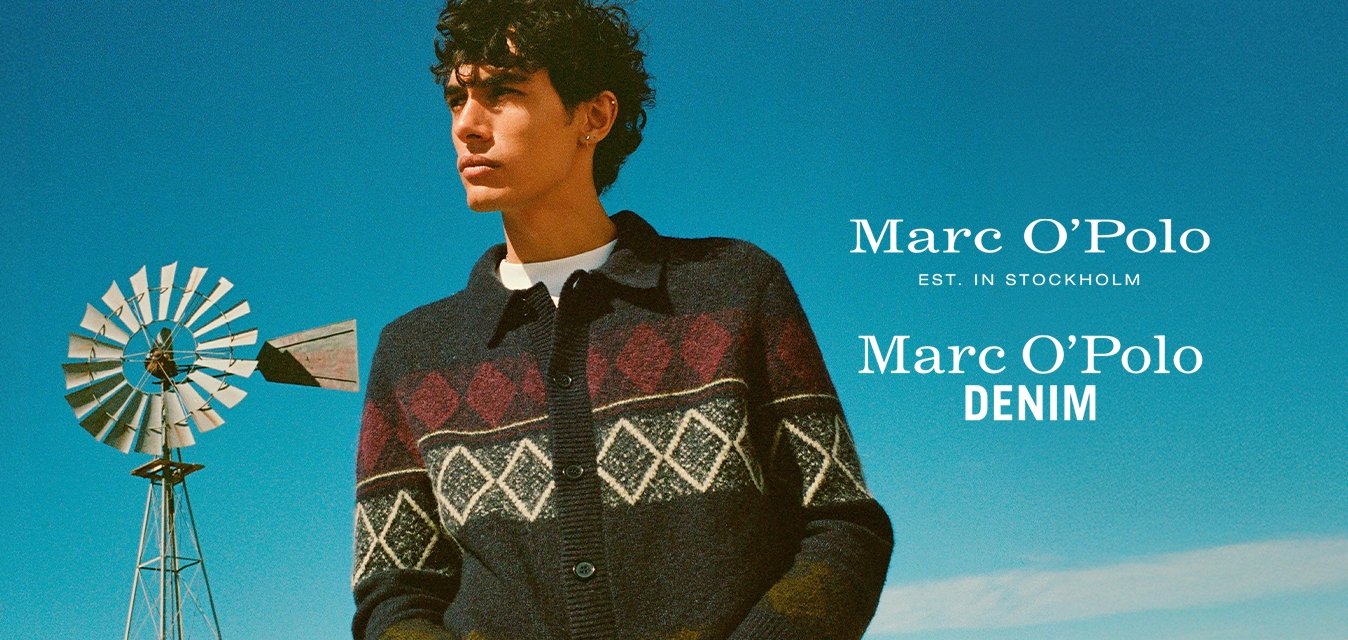 Cardigan navy con diamanti rossi e bianchi a motivo, chiusura a bottoni, design con colletto e maniche a coste. Il modello si trova in piedi contro un cielo blu.