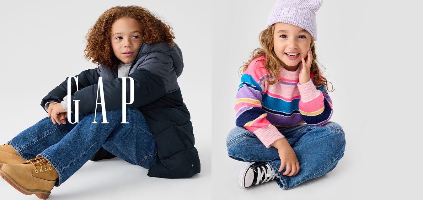 Due bambini seduti su uno sfondo neutro. Uno indossa una giacca imbottita scura e jeans azzurri; l'altro porta un maglione a righe e un berretto lavanda.