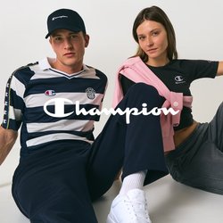 Un uomo e una donna sono seduti per terra contro una parete bianca, entrambi indossano abbigliamento casual Champion e mantengono pose rilassate.