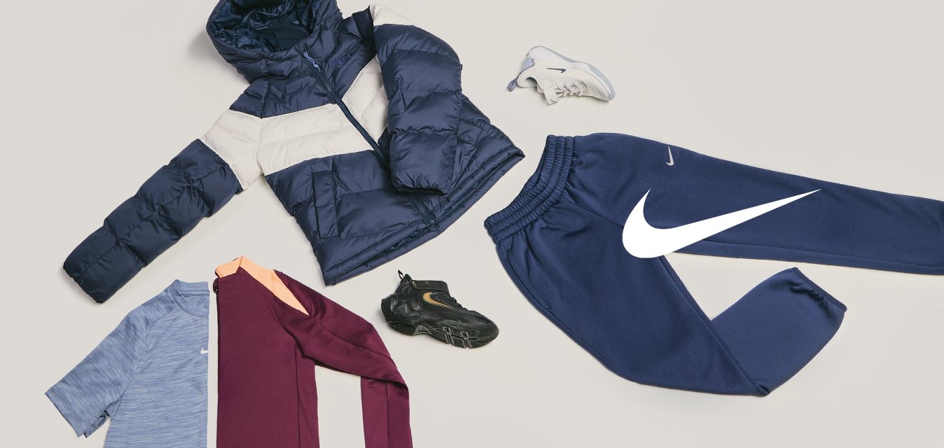 Giacca imbottita blu scuro e beige, camicie blu e bordeaux, pantaloni della tuta blu scuro, scarpe da ginnastica nere e bianche disposti su sfondo chiaro.