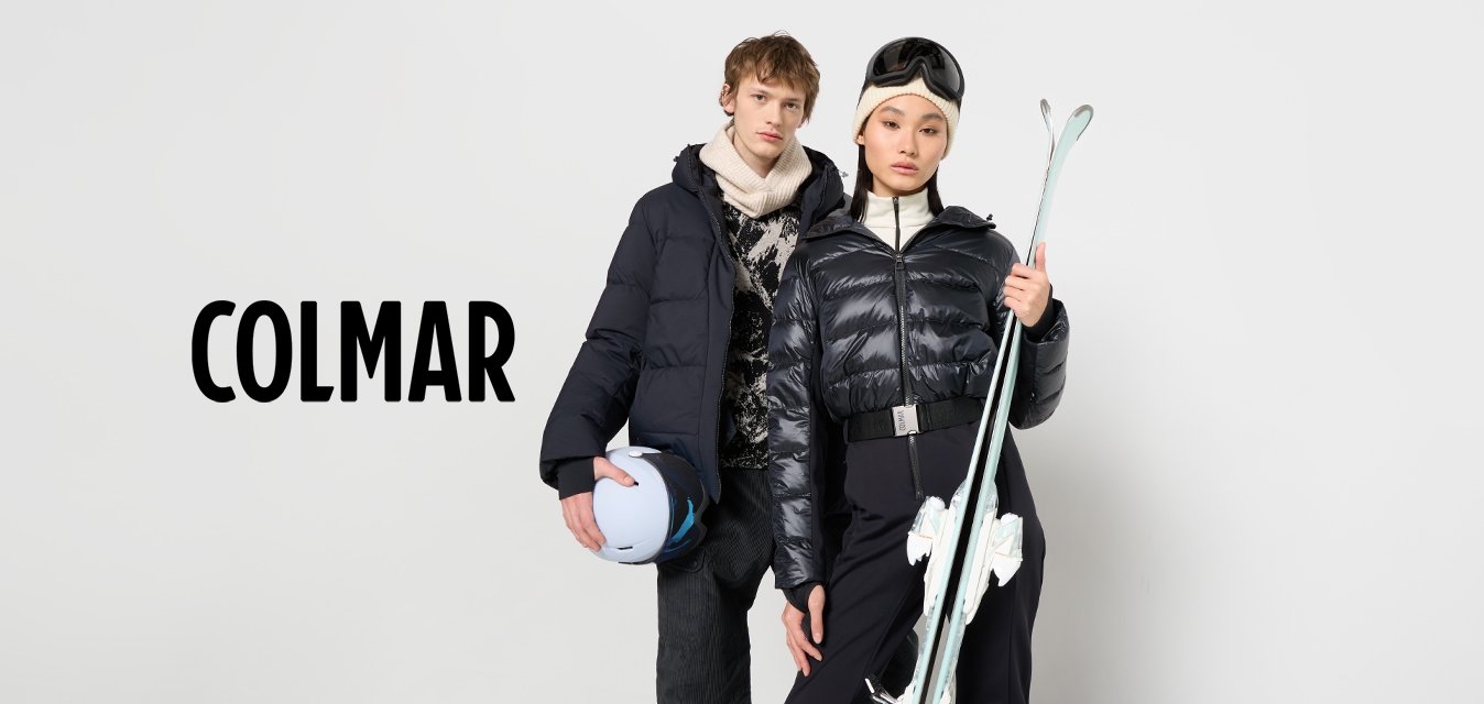 Giubbotti neri gonfi con zip, dolcevita crema e attrezzatura da sci. Uno tiene un casco blu, l'altro sci bianchi, su uno sfondo semplice.