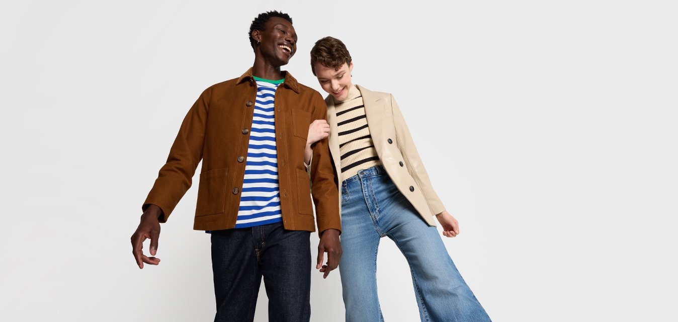 Due modelli stanno fianco a fianco. Uno indossa una giacca marrone sopra una camicia a righe blu e bianche; l'altro indossa un blazer beige a righe verticali e jeans a zampa d'elefante.