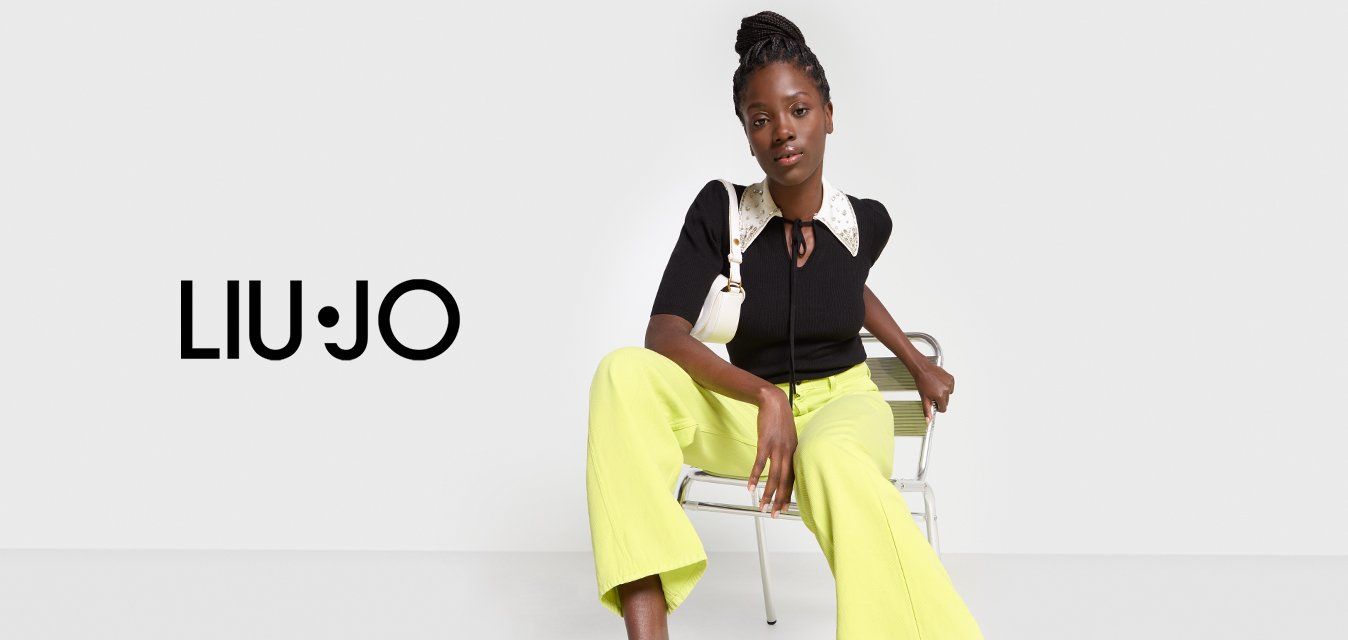 Top nero a costine con colletto bianco decorato e cravattino, abbinato a pantaloni larghi gialli e tacchi neri con straps.